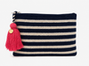 A crochet zip pouch with horizontal navy blue and cream stripes, featuring a bright pink tassel charm with a gold-tone circular brand tag, set against a plain white background.