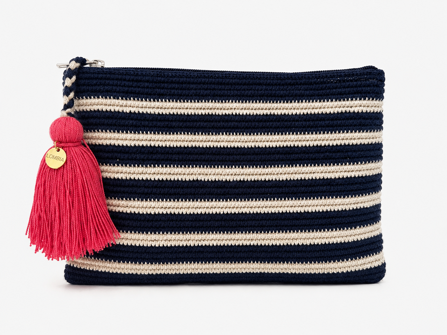 A crochet zip pouch with horizontal navy blue and cream stripes, featuring a bright pink tassel charm with a gold-tone circular brand tag, set against a plain white background.