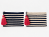 Two woven zip pouches with red & pink tassels, shown side by side on a white background. The left pouch is navy blue & has cream horizontal stripes, and the right pouch is beige and has navy horizontal stripes.