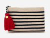 A woven rectangular crochet clutch bag in beige with horizontal stripes in navy blue, featuring a large red tassel with a gold round charm on the zipper pull.